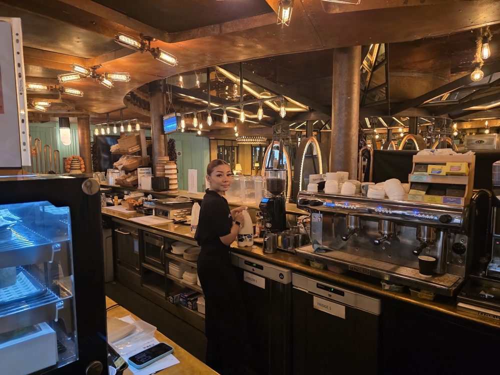 The service counter and espresso setup along one wall of The Holmes Cafe, with a chilled display cabinet at the near end