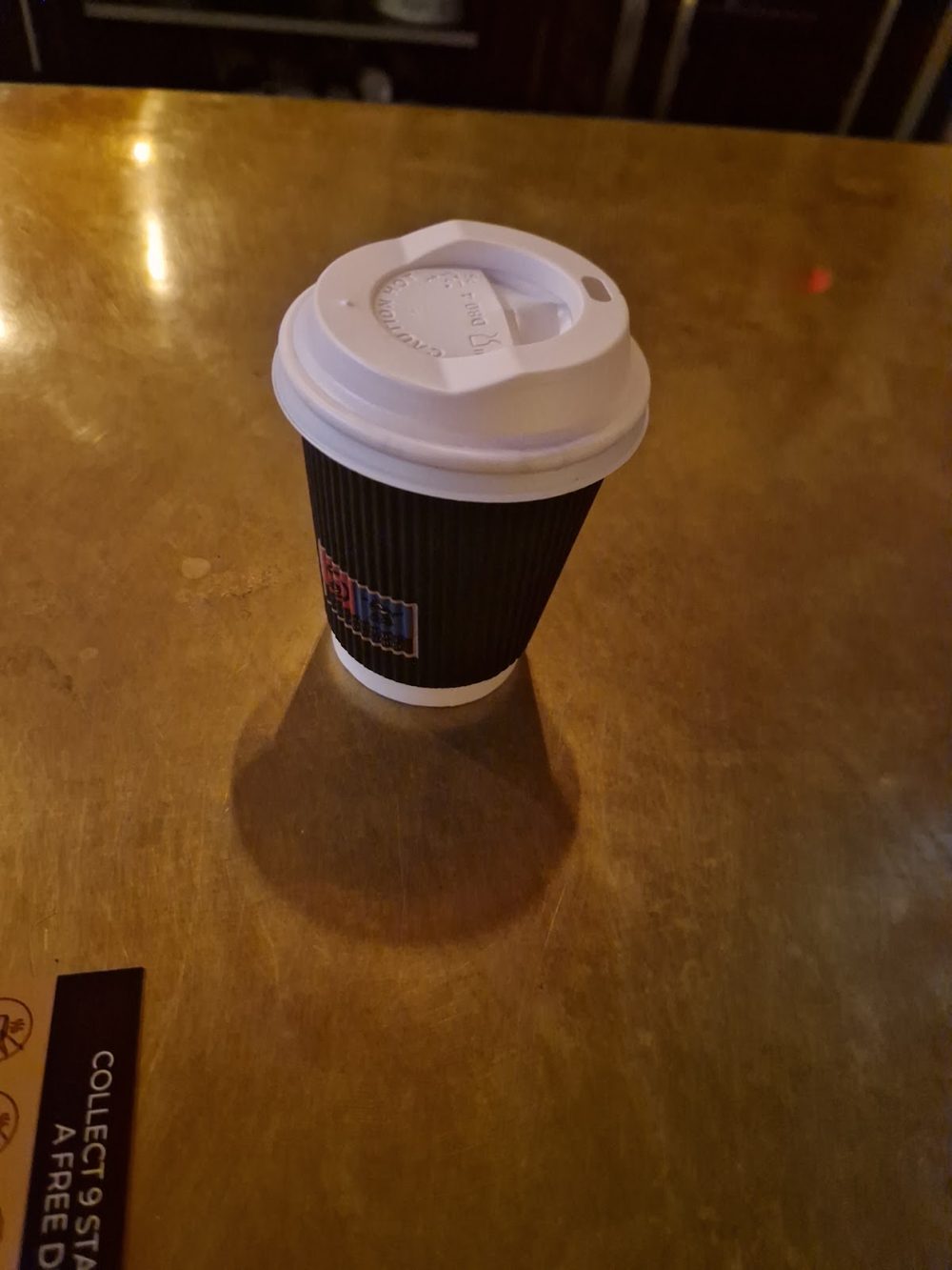 A takeaway coffee cup on a bare wooden table, cropped to remove the burned-in wording
